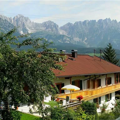A cozy house in nature with a view of impressive mountains. The surroundings are green and inviting.