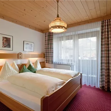 A cozy bedroom with two beds and wooden paneling. Large windows let in a lot of daylight and the carpet is red.