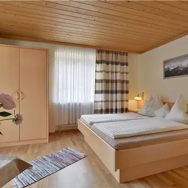 A cozy bedroom with a wooden ceiling and two beds. Designed with a wardrobe and a flower arrangement on the table.