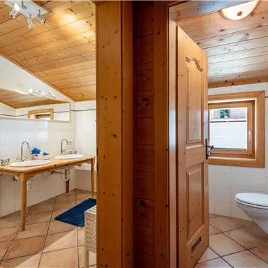 A modern bathroom with wooden paneling and two sinks. There is a window and a clear, bright atmosphere.