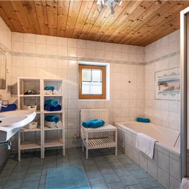 A modern bathroom with light tiles and a wooden ceiling. The amenities include a sink, a bathtub, and a shower.