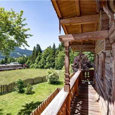 A beautiful view from a balcony overlooking a green meadow and trees. The mountain landscape in the background creates a relaxed atmosphere.