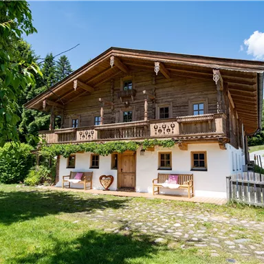 A traditional wooden house in alpine style with a large balcony.  
Surrounded by lush greenery and trees, it conveys a cozy atmosphere.