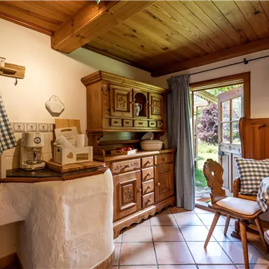 A cozy kitchen with wooden cabinets and a large window that lets in light. The room is furnished with a checkered tablecloth and country-style decorations.