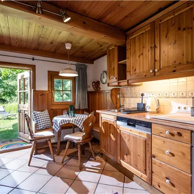 A cozy wooden kitchen with a dining table and chairs. A window opens up to a green garden.