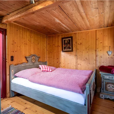 A cozy bedroom with wooden paneled walls and a large bed. The decor is rustic with a traditional nightstand and decorative elements.
