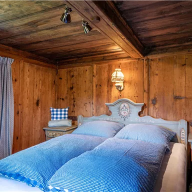 A cozy bedroom with wood paneling and blue bedspreads. The decor is rustic with a window, curtains, and decorative pillows.