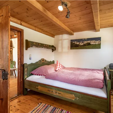 A cozy bedroom with a wooden bed and red bedding. The room has wooden paneling and a window with curtains.