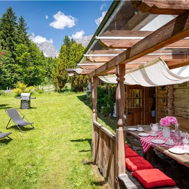 A charming terrace with wooden furniture and blooming flowers. In the background, there is a green lawn with loungers and lush vegetation.