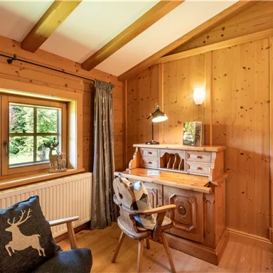 A cozy wood interior with a desk, a chair, and a window that offers a view of the garden. A wall clock complements the warm atmosphere of the room.