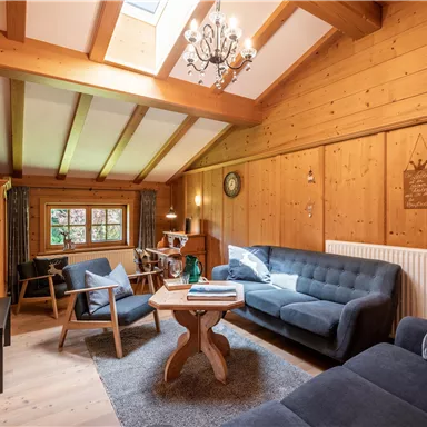 A cozy living room with wooden paneling and bright furniture. Large windows provide plenty of light and an inviting atmosphere.