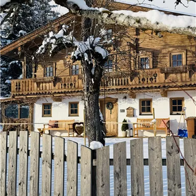 A cozy wooden house in the snow, surrounded by a wooden picket fence. The scene conveys a calm winter atmosphere.