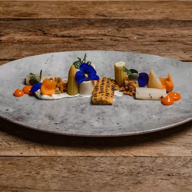 An artistically arranged plate with colorful vegetables and edible flowers. The arrangement is creative and appealing on a rustic wooden surface.