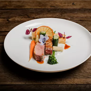 A beautifully arranged plate with meat, colorful vegetables, and a decorative flower. The vibrant colors make the dish enticing.
