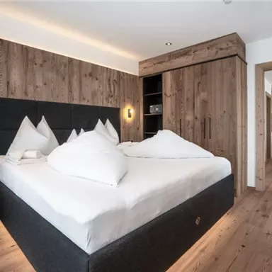 Ein modernes Schlafzimmer mit einem großen Doppelbett und Holzverkleidung. Die warmen Holztöne schaffen eine gemütliche Atmosphäre.