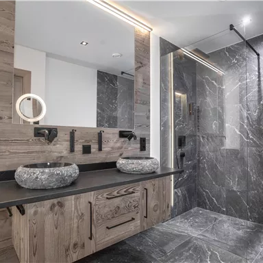 Ein modernes Badezimmer mit einer Kombination aus Holz- und Steinoberflächen. Die großzügige Dusche und die eleganten Waschbecken aus Stein verleihen dem Raum eine luxuriöse Atmosphäre.