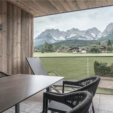 Ein moderner Balkon mit Stühlen und Tisch bietet einen spektakulären Blick auf die Berge. Die Umgebung ist grün und einladend, ideal zum Entspannen.