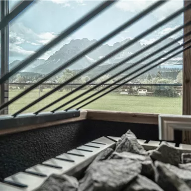Ein moderner Innenraum mit Blick auf eine grüne Wiese und die Berge im Hintergrund. Steine sind im Vordergrund sichtbar, die die natürliche Umgebung betonen.