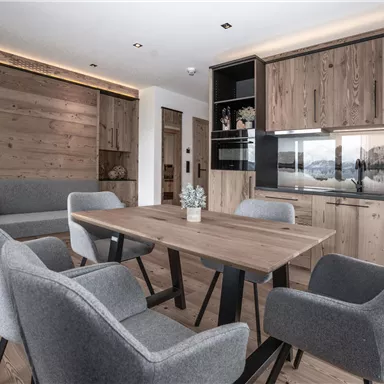 Ein modernes Esszimmer mit einem Holztisch und bequemen Stühlen. Die Wände sind aus Holz, und die Küche ist elegant und gut ausgestattet.