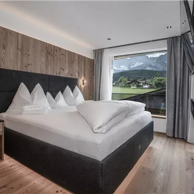 Ein modernes Hotelzimmer mit einem großen Doppelbett und Waldblick. Die Wände sind aus Holz, und das Zimmer ist hell und einladend.