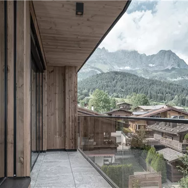 Ein moderner Balkon mit Holzverkleidung und Blick auf grüne Berge. Die Landschaft ist von einer ruhigen und natürlichen Atmosphäre geprägt.