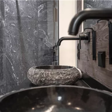 Ein modernes Badezimmer mit eleganten schwarzen Waschbecken und stilvollen Wasserhähnen. Die Wände sind in einem schlichten grauen Design gehalten.