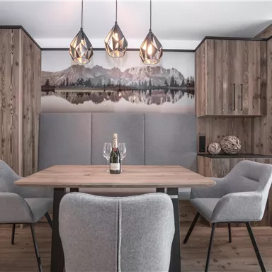 Ein modernes Esszimmer mit einem Holztisch und gemütlichen Stühlen. Die Wände sind in warmen Holzfarben gehalten, und über dem Tisch hängen stilvolle Lampen.