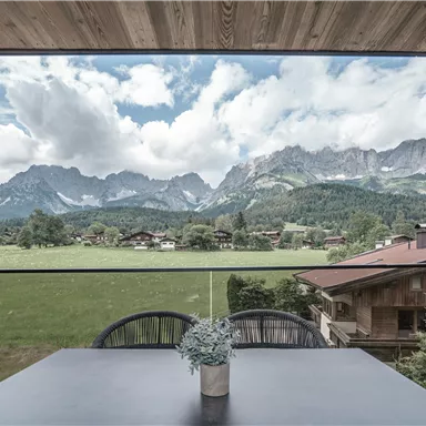 Ein Blick auf die majestätischen Berge mit einer wunderschönen Wolkenlandschaft. Im Vordergrund steht ein Tisch mit einer Blumenvase, der eine gemütliche Atmosphäre schafft.