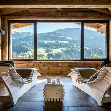 A cozy room with two lounges and a small table. Through large windows, one looks out at a picturesque mountain landscape.