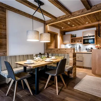 A modern, cozy dining room with a wooden table and chairs. The warm wood surfaces and indirect lighting create an inviting atmosphere.