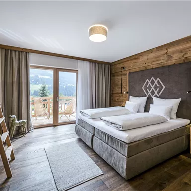 A modern bedroom with wooden details and two beds. In the background, there are windows with a view of nature.
