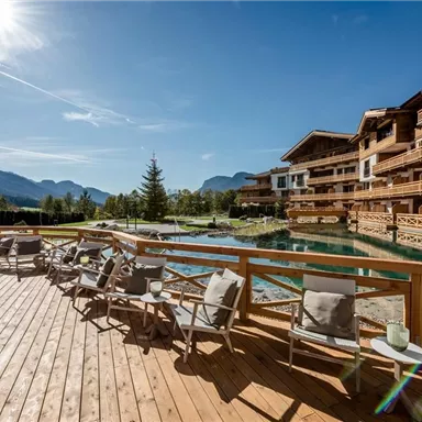 A sunny day on a terrace overlooking a hotel and beautiful scenery. Chairs invite you to relax by the water.