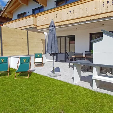 A cozy terrace with a grill and sun loungers. Surrounded by a well-maintained lawn and modern wooden cladding.