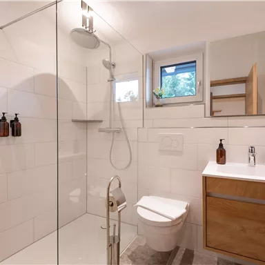 A modern bathroom with a shower and a wooden sink. Large tiles and a window create a bright atmosphere.