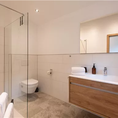 A modern bathroom with a glass shower and a wooden cabinet. Fresh towels and toiletries are visible.