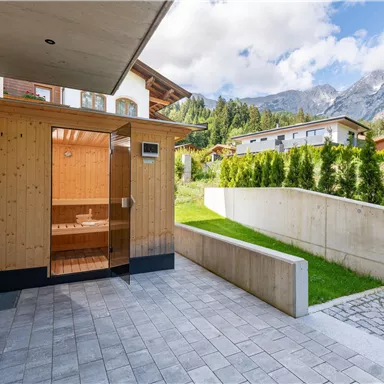 A modern sauna area made of wood in a beautiful garden. In the background, mountains and a clear sky are visible.