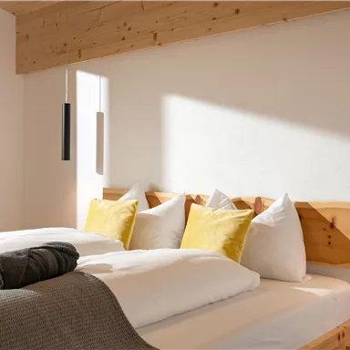 A cozy bedroom with a double bed and yellow cushions. Soft light falls on the wooden walls and the modern decoration.