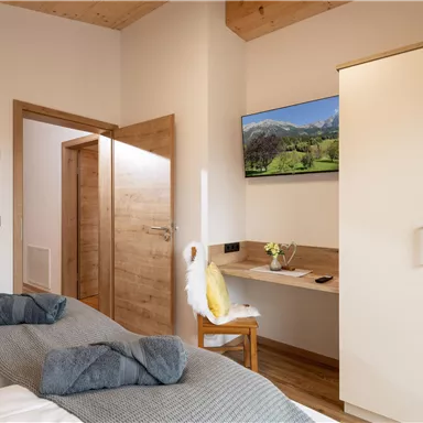A modern bedroom with two single beds and a desk. A TV is mounted on the wall and there is a door to another room.