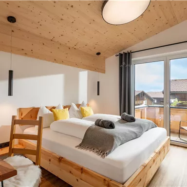 A modern bedroom with wooden walls and a large window. There is a cozy bed and a wooden chair that creates a relaxing atmosphere.