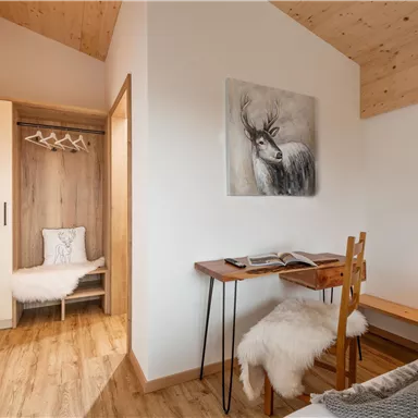 A bright room with wooden floors and modern furnishings. On a small table, there is a book, next to it a chair with a cozy fur.