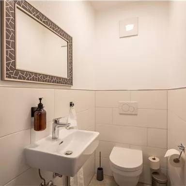 A modern bathroom with a sink and a toilet. There is a mirror on the wall and the tiles are light and simple.