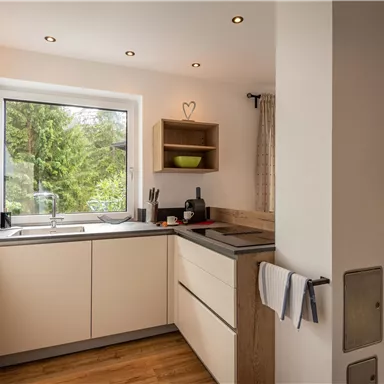 A modern kitchen with bright cabinets and a large window. The room has a warm atmosphere and a view of the garden.