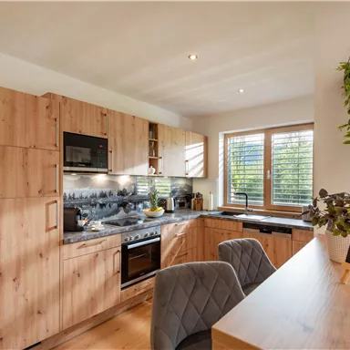 Eine moderne Küche mit Holzregalen und Geräten. Der Raum ist hell und einladend, mit einer kleinen Tafel, die „Willkommen!“ sagt.