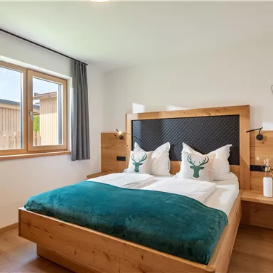 Ein gemütliches Schlafzimmer mit einem großen Bett und Holzdetails. Der Raum hat ein Fenster mit Blick nach draußen und dekorative Kissen.