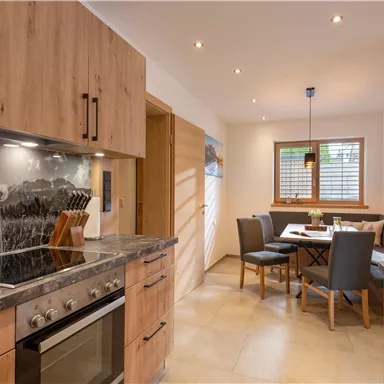 Eine moderne Küche mit Holzschränken und einer Kochstelle. Im Hintergrund befindet sich ein Essbereich mit einem Tisch und Stühlen.