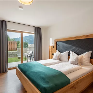 Ein modernes Schlafzimmer mit einem Doppelbett und einer gemütlichen Ausstattung. Große Fenster bieten einen Blick auf den Garten.