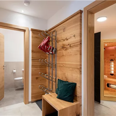 Ein moderner Eingang mit Holzverkleidung und einer Sitzgelegenheit. Auf der rechten Seite befindet sich eine Sauna, während im Hintergrund eine Tür zu einem Badezimmer sichtbar ist.