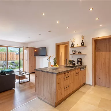 Eine moderne Küche mit Holzschränken und einer Insel. Der Raum ist hell und freundlich mit Zugang zu einem Garten.