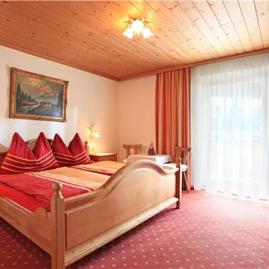 A cozy bedroom with a double bed and red pillows. Large windows provide plenty of natural light.