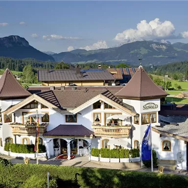 A charming building in alpine style, surrounded by green meadows and mountains. The architecture is traditional with turrets and balconies.